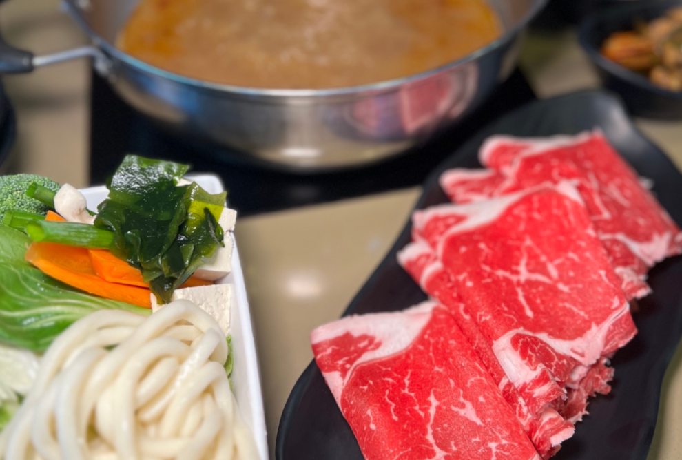 shabu shabu soup with bowl of veggies on the left and marbled prime rib eye on the right