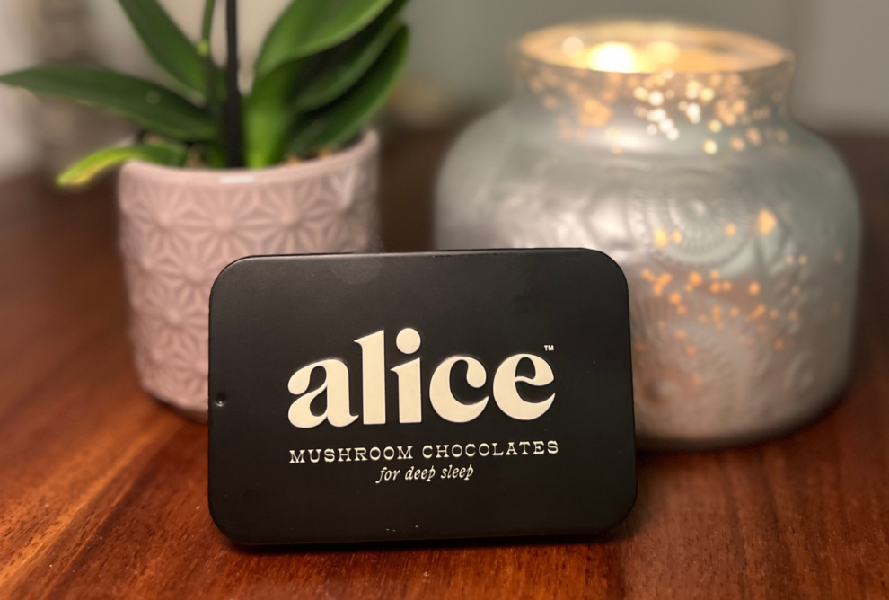 alice mushrooms tin with a silver candle on the right background and a plant on the left background